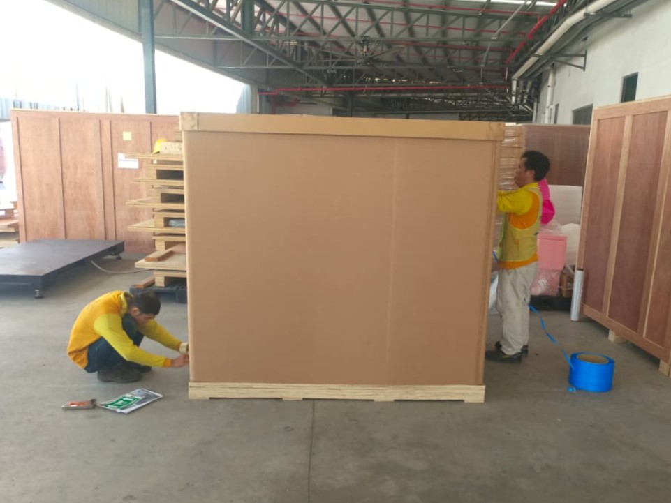 An M&C worker sealing a large heavy-duty industrial cardboard crate in the warehouse