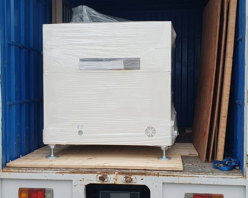 A large white industrial machine wrapped and secured inside an M&C delivery lorry